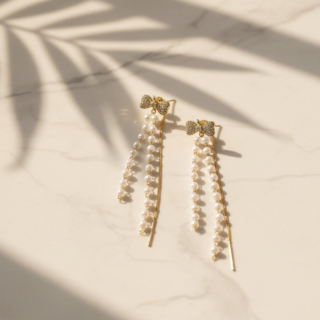 SVORA gold tone dangle earrings with pavé bow tops and cascading freshwater-style pearls and chains.