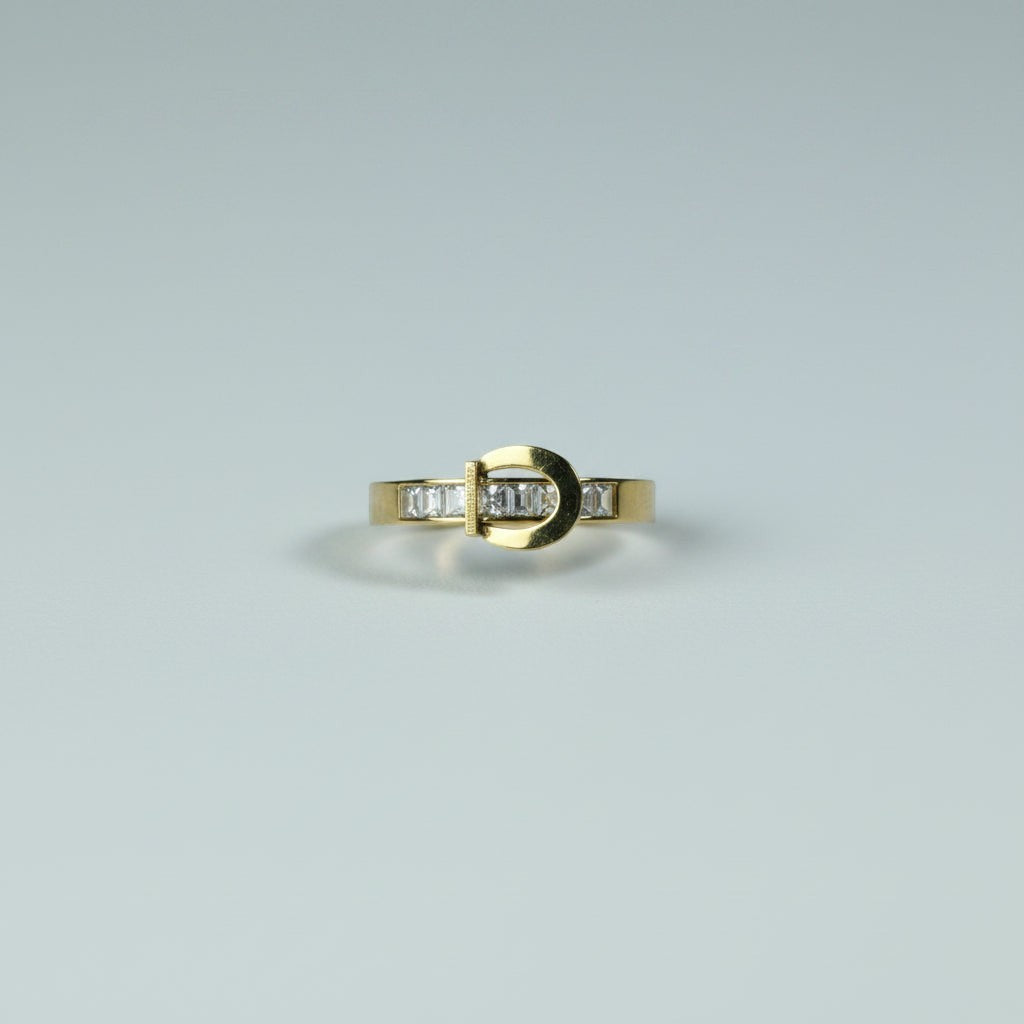 SVORA gold tone stainless steel ring with channel-set baguette cubic zirconia stones in a buckle design.
