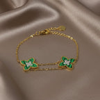 SVORA gold double chain bracelet with two green clover charms, each with a small CZ center. Adjustable.