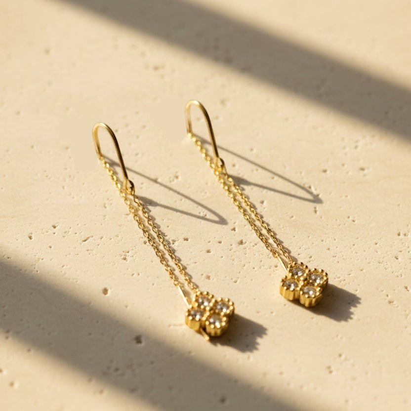 SVORA gold tone stainless steel dangler earrings with cubic zirconia clover charms and delicate chains.