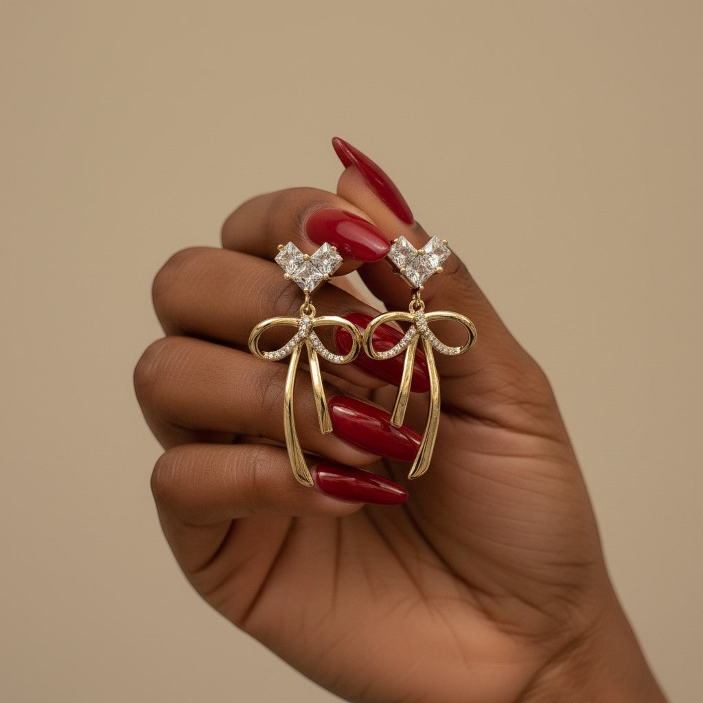 SVORA gold-tone drop earrings with crystal heart tops and bow charms, featuring 18k gold plating and cubic zirconia.