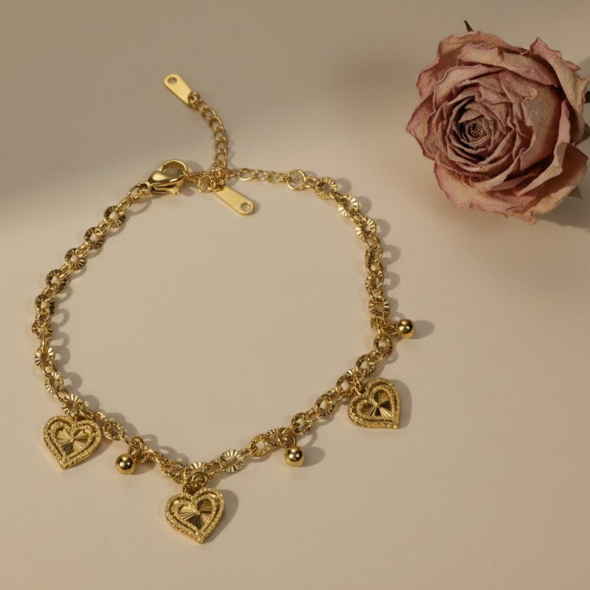 SVORA gold cable chain bracelet with three suspended heart charms and gold beads. Adjustable with lobster clasp.