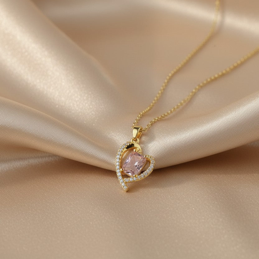 SVORA gold heart necklace with pink crystal center and small clear crystals on the outline, on a satin background.