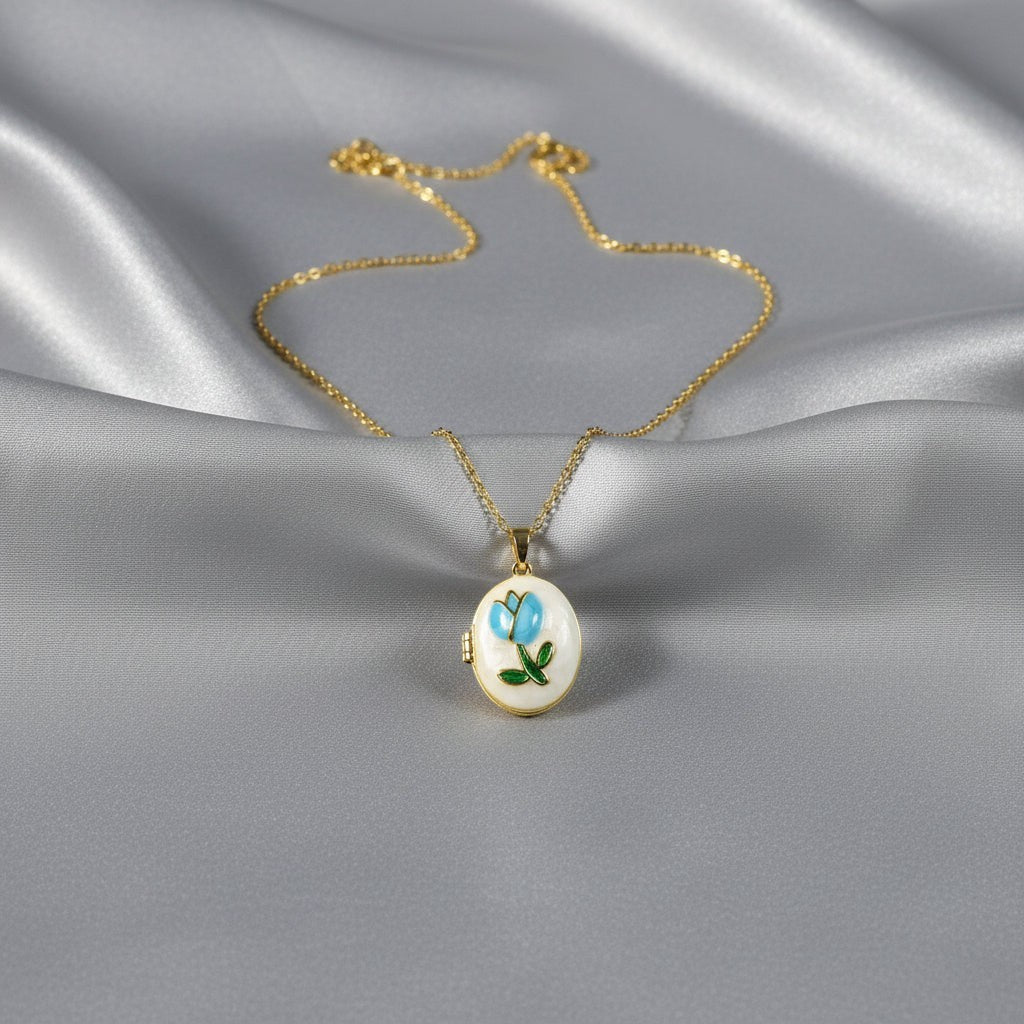 SVORA gold plated stainless steel locket necklace with a blue rose and green leaf enamel design on a mother-of-pearl disc.