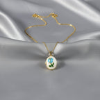 SVORA gold plated stainless steel locket necklace with a blue rose and green leaf enamel design on a mother-of-pearl disc.