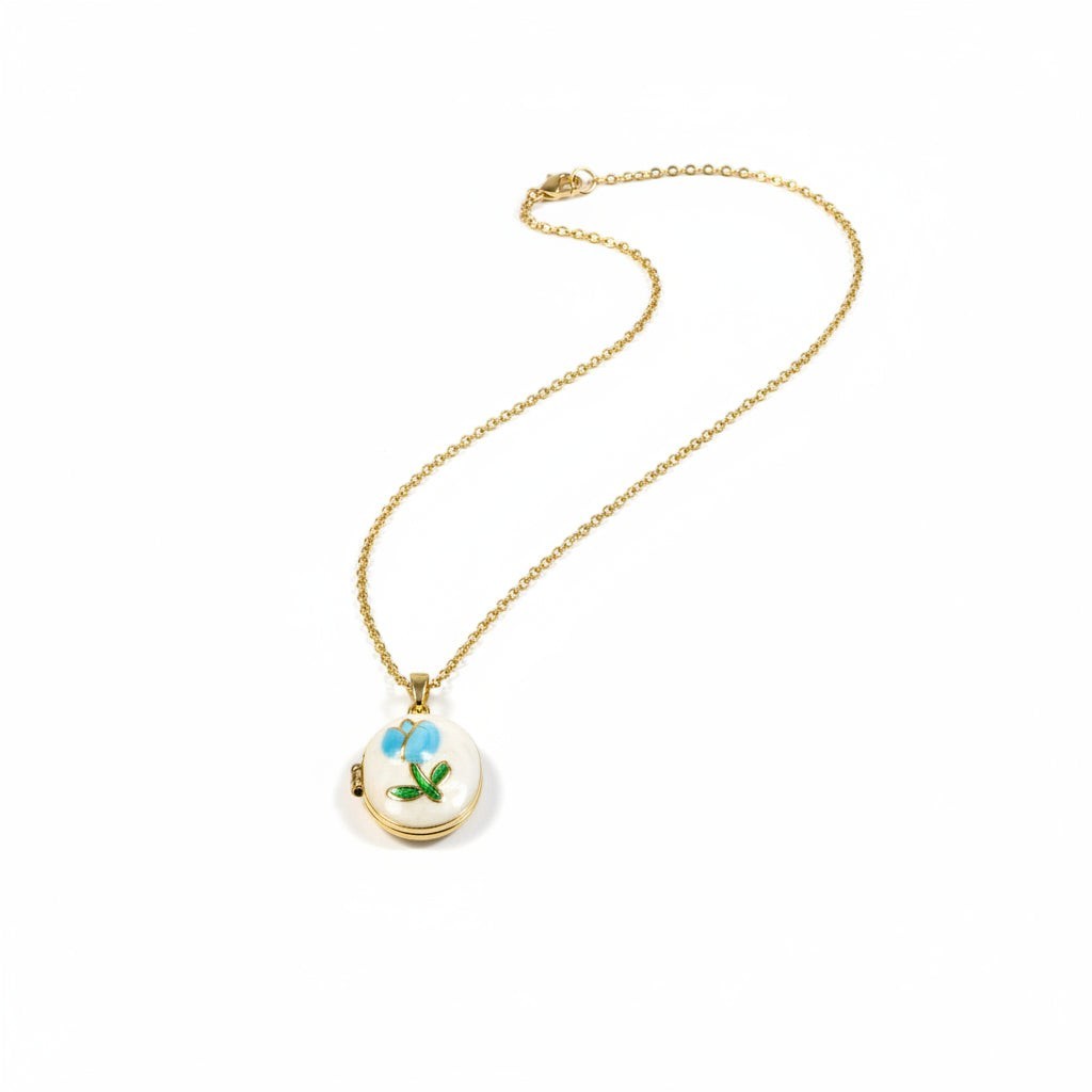 SVORA gold locket necklace with mother-of-pearl disc, blue enamel rose, and green leaf detail. 18K gold plated.