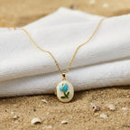 SVORA gold plated stainless steel locket necklace with mother-of-pearl, blue enamel rose, and green leaf design.