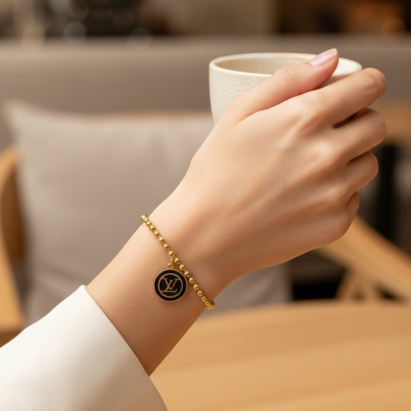 SVORA gold ball bead chain bracelet with black monogram disc charm. 18K gold plated, adjustable.