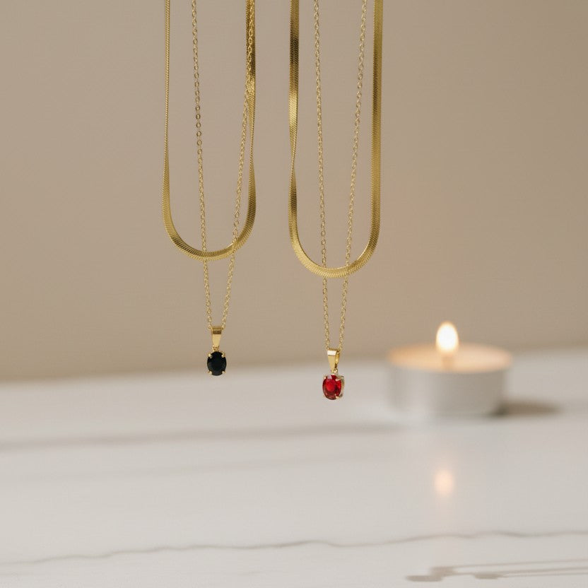 SVORA gold necklace with black oval crystal pendant on a snake chain. Layered with another gold chain.