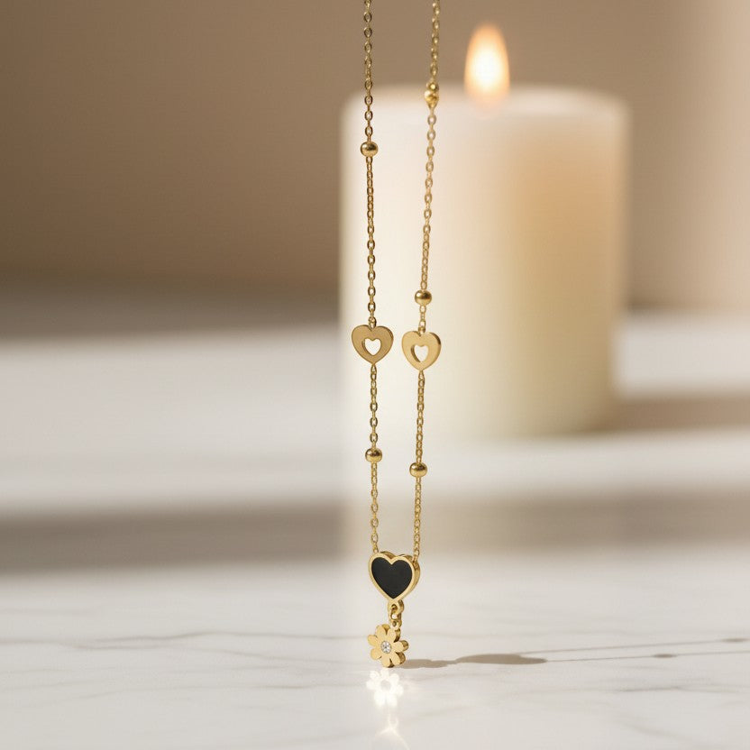 SVORA gold necklace with black enamel heart, daisy charm, and hollow heart details. Stainless steel, 18k gold plated.