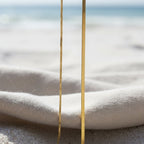 SVORA gold snake chain necklace and box chain necklace on a beach with soft fabric and sand.