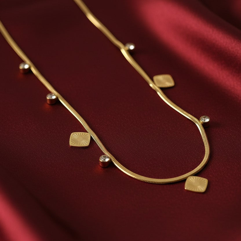 SVORA gold snake chain necklace with square charms and clear stone accents. 18k gold plated stainless steel.