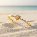 SVORA gold-plated stainless steel bracelet with a central solitaire CZ stone and floral design, set on a sandy beach.