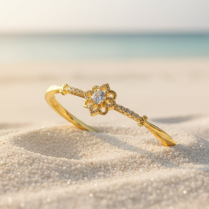 SVORA gold-plated stainless steel bracelet with a central solitaire CZ stone and floral design, set on a sandy beach.