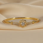 SVORA gold-plated stainless steel hinged bracelet with a central flower design featuring a clear cubic zirconia and smaller CZ accents.