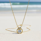 SVORA gold plated stainless steel solitaire pendant necklace with pavé butterfly detail on a beach.