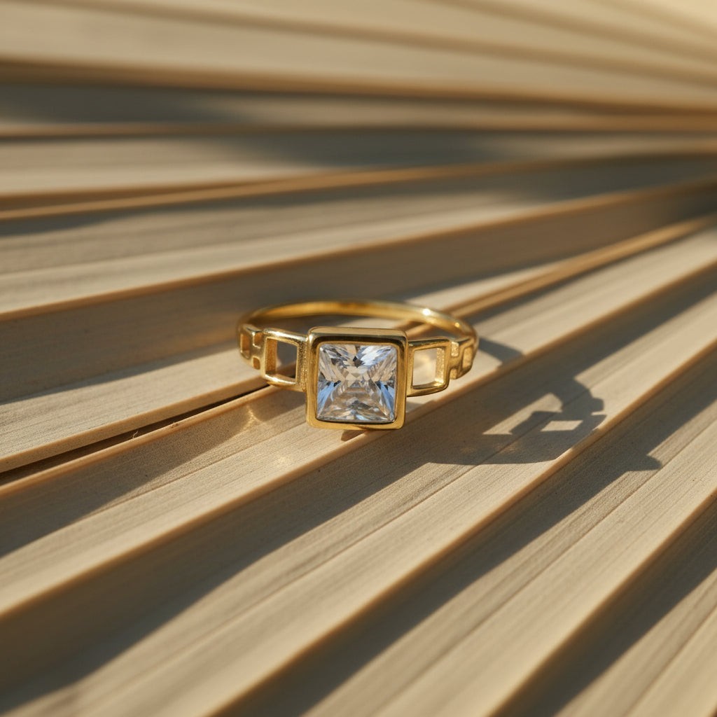 SVORA gold plated stainless steel ring with a square-cut clear stone and geometric band detail.