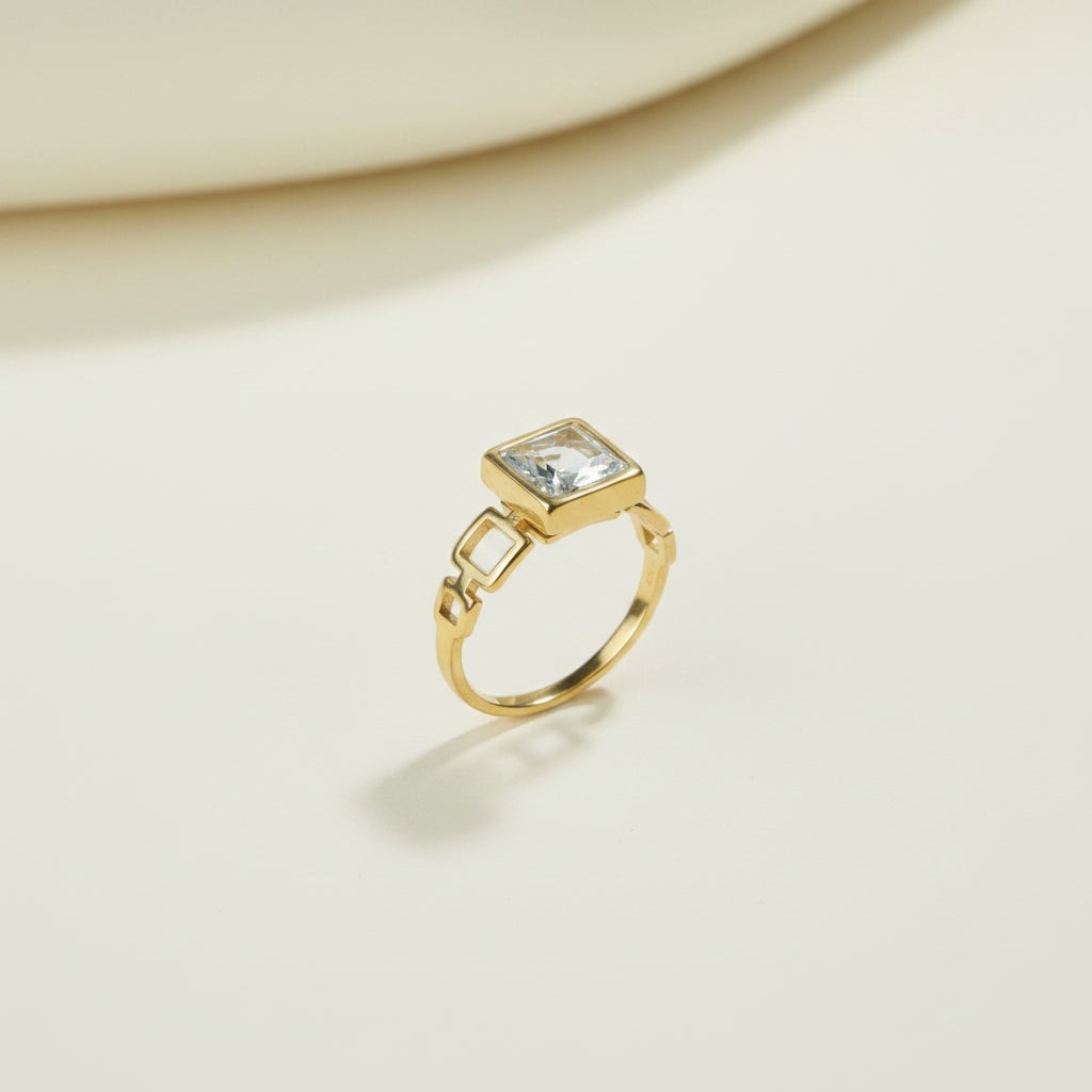 SVORA gold plated stainless steel ring with a square-cut clear stone and geometric links.
