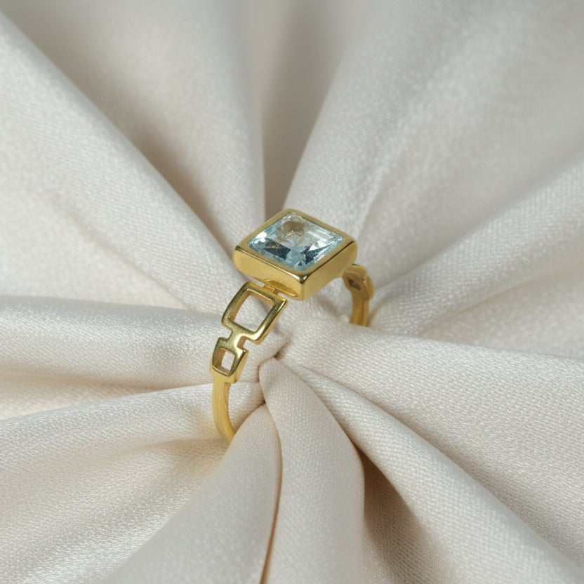 SVORA gold plated stainless steel ring with a square-cut aquamarine stone and geometric band.