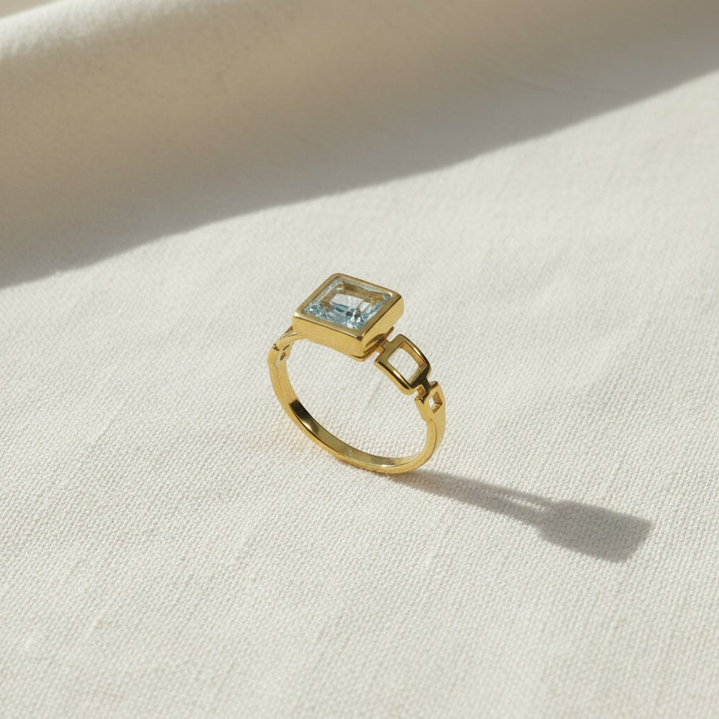 SVORA gold ring with a square-cut blue stone and open square link band. 18K gold plated stainless steel.