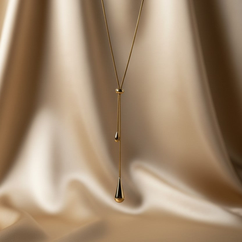 SVORA gold teardrop lariat necklace with adjustable snake chain and polished charms on a satin background.