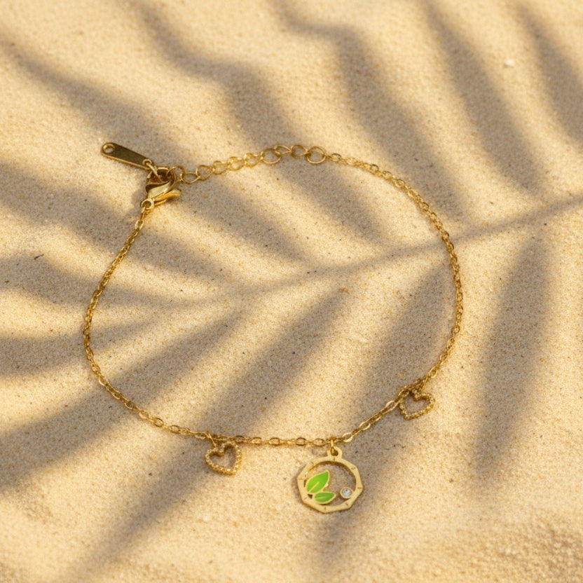SVORA gold chain bracelet with green leaf charm, two small hearts, and a cubic zirconia stone. Adjustable.
