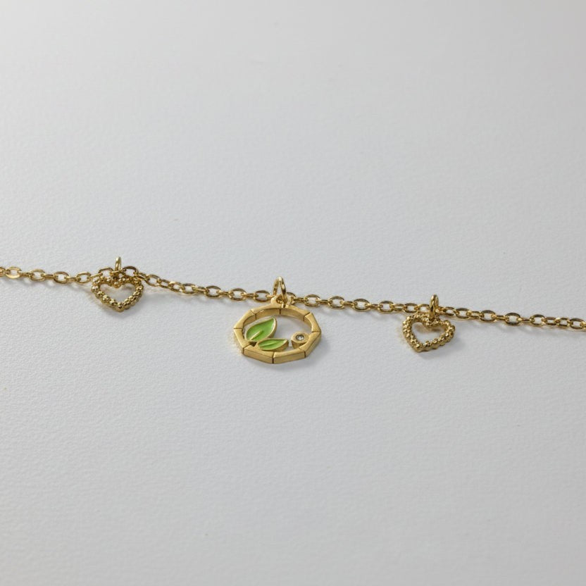 SVORA gold chain bracelet with green leaf charm, two heart charms, and a small cubic zirconia stone.