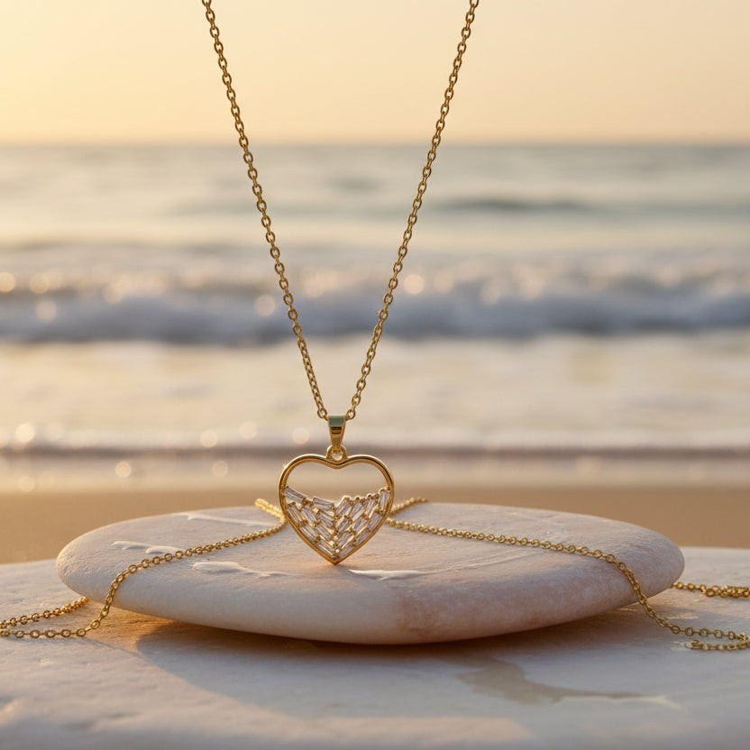 SVORA gold plated stainless steel necklace with a heart pendant filled with baguette CZ stones. Beach background.