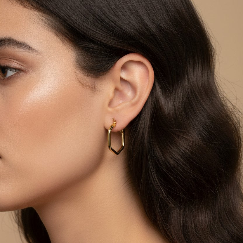 SVORA gold-tone stainless steel hexagon hoop earrings with a polished finish, worn by a model.