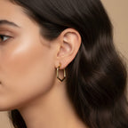 SVORA gold-tone stainless steel hexagon hoop earrings with a polished finish, worn by a model.