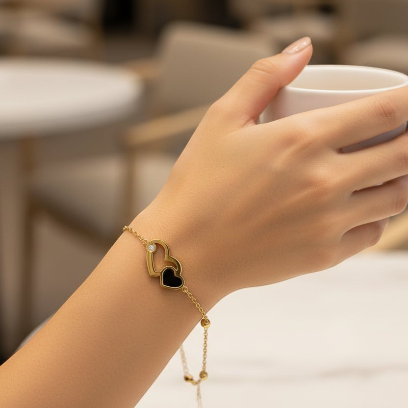 SVORA gold plated stainless steel bracelet with interlocking hearts, one black and one open with a CZ.