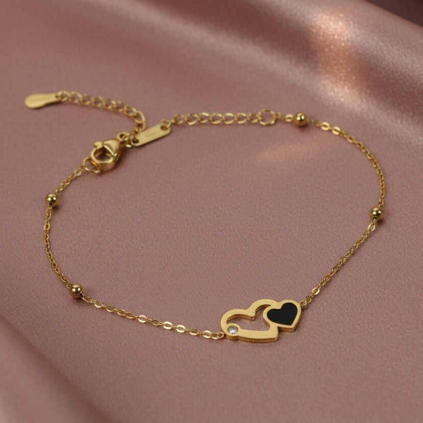 SVORA gold chain bracelet with interlocking hearts, one black and one outlined with a CZ stone.