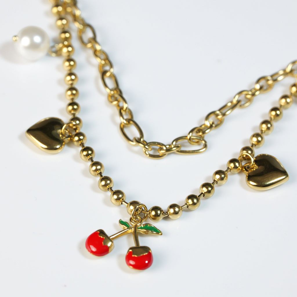 SVORA gold layered necklace with paperclip and ball-bead chains, featuring pearl, heart, and cherry charms.