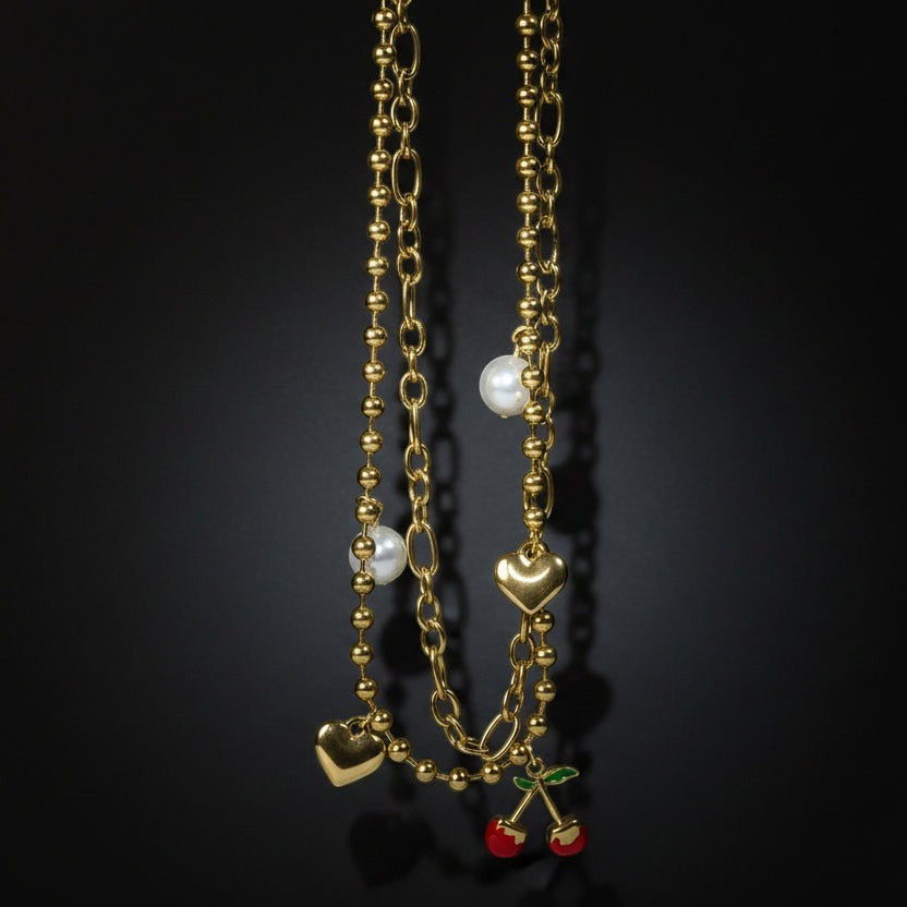 SVORA gold layered necklace with paperclip and ball-bead chains, pearls, hearts, and cherry charm.