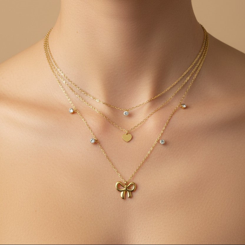 SVORA layered gold necklace with bow, heart, and solitaire charms. 18k gold-plated stainless steel.