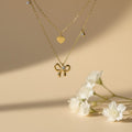 SVORA layered gold necklace with bow, heart, and solitaire charms. 18k gold-plated stainless steel.