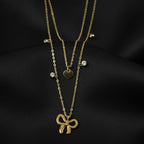 SVORA layered gold necklace with bow, heart, and solitaire charms on a black satin background.