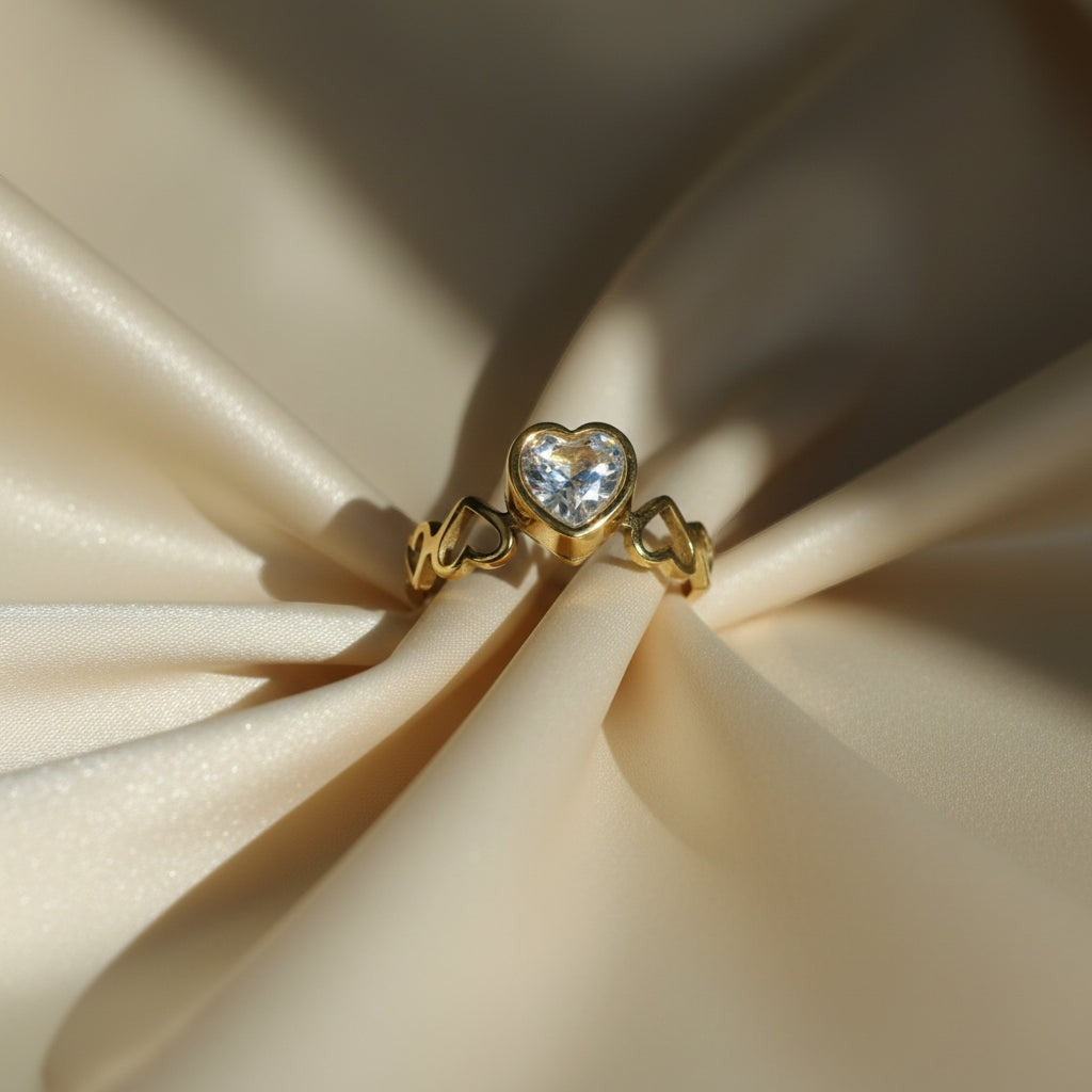 SVORA Lumiere Amour gold heart ring with clear cubic zirconia center stone and heart details on band.