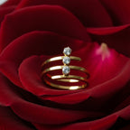 SVORA gold tone stainless steel spiral ring with three cubic zirconia stones, set on a red rose petal.