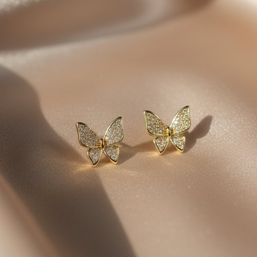 SVORA mini gold tone butterfly stud earrings with cubic zirconia stones on a satin background.