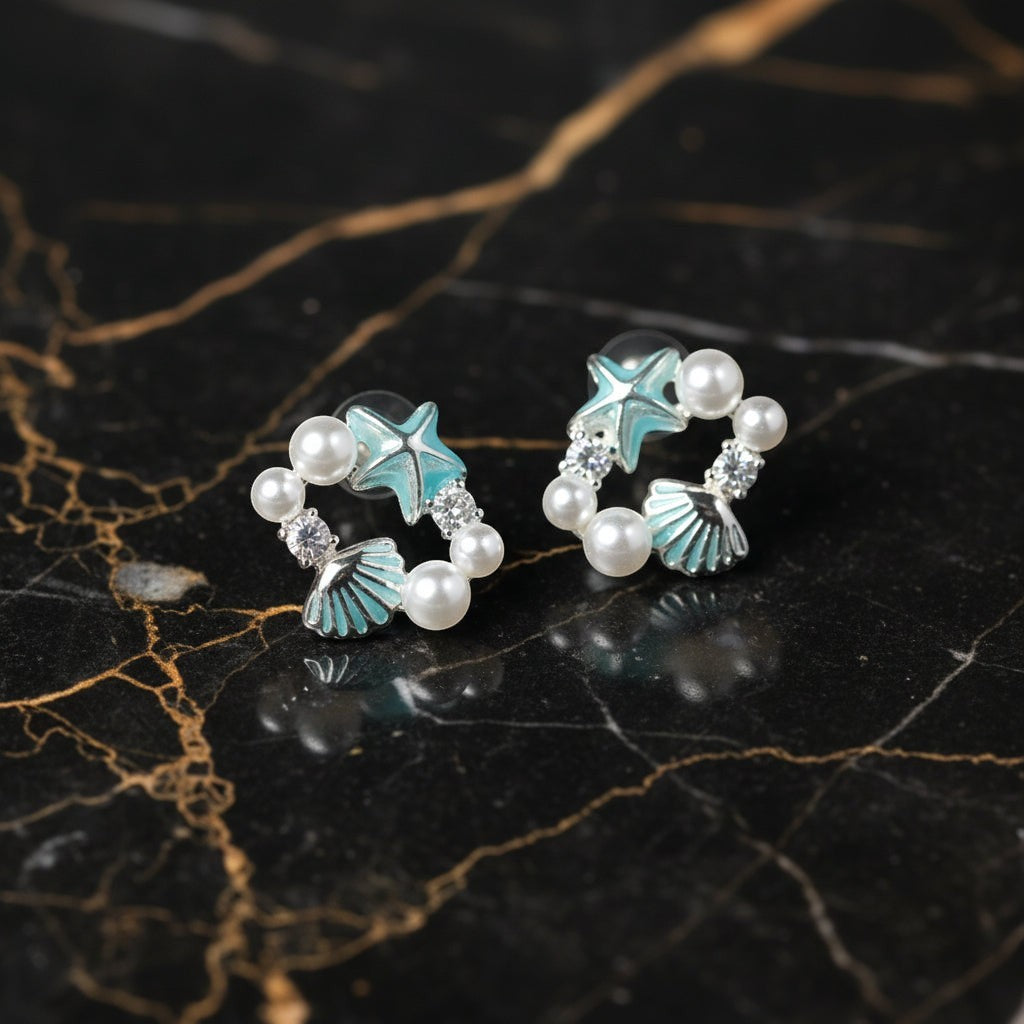 SVORA Ocean Cluster Pearl Stud Earrings with aqua starfish, shell, pearls, and cubic zirconia on a marble background.