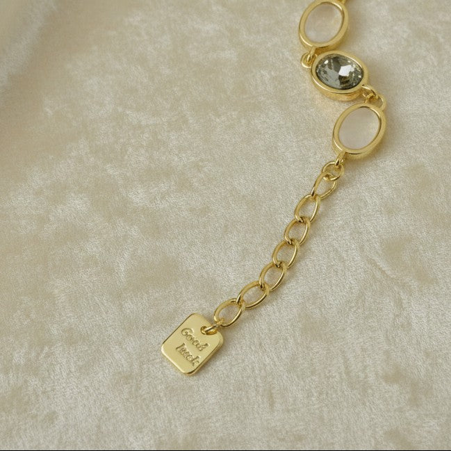 SVORA gold-tone adjustable bracelet with oval opal grey gemstones and a good luck charm.