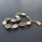 SVORA gold-tone bracelet with alternating opal and grey oval gemstones and a good luck charm.