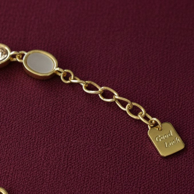 SVORA gold-tone adjustable bracelet with oval opal pink gemstones and a square 'Good Luck' charm.