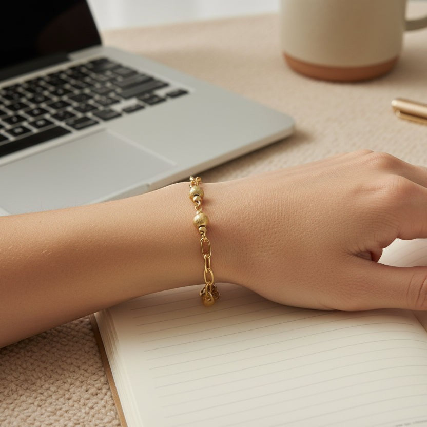 SVORA gold paperclip chain bracelet with textured beads on a woman's wrist, styled with a laptop and notebook.