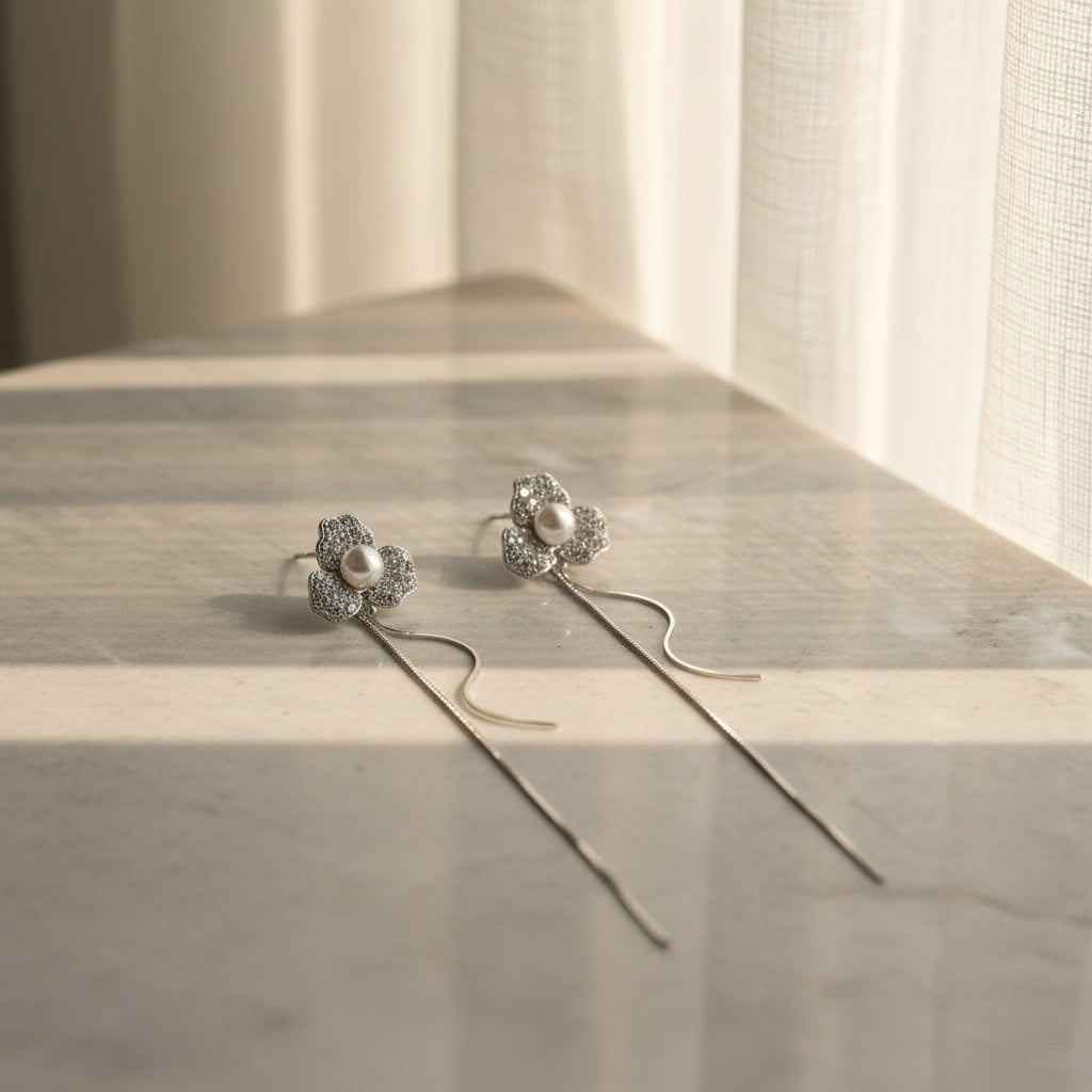 SVORA silver-tone stud earrings with three pavé-set cubic zirconia petals and a central pearl, featuring delicate chain tassels.