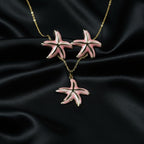 SVORA pink enamel starfish necklace and matching earrings set with gold-tone accents on a black satin background.