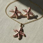 SVORA pink enamel starfish necklace and matching earrings set with gold-tone accents on a gold chain.