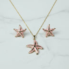 SVORA pink enamel starfish necklace and matching earrings with gold trim, set on a marble background.