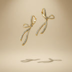 SVORA gold-tone stainless steel dangle earrings with diamond-like accents in a ribbon knot design.
